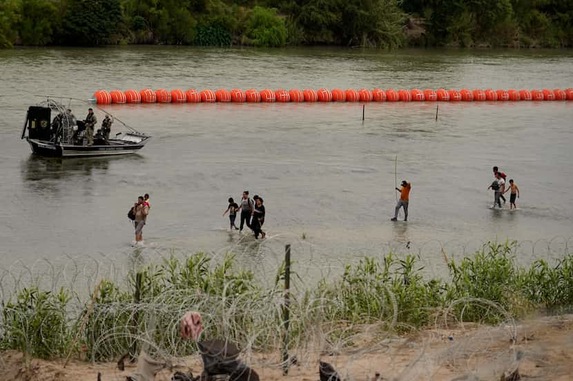 Migrants who crossed the Rio Grande from Mexico walk past large buoys being deployed as a...