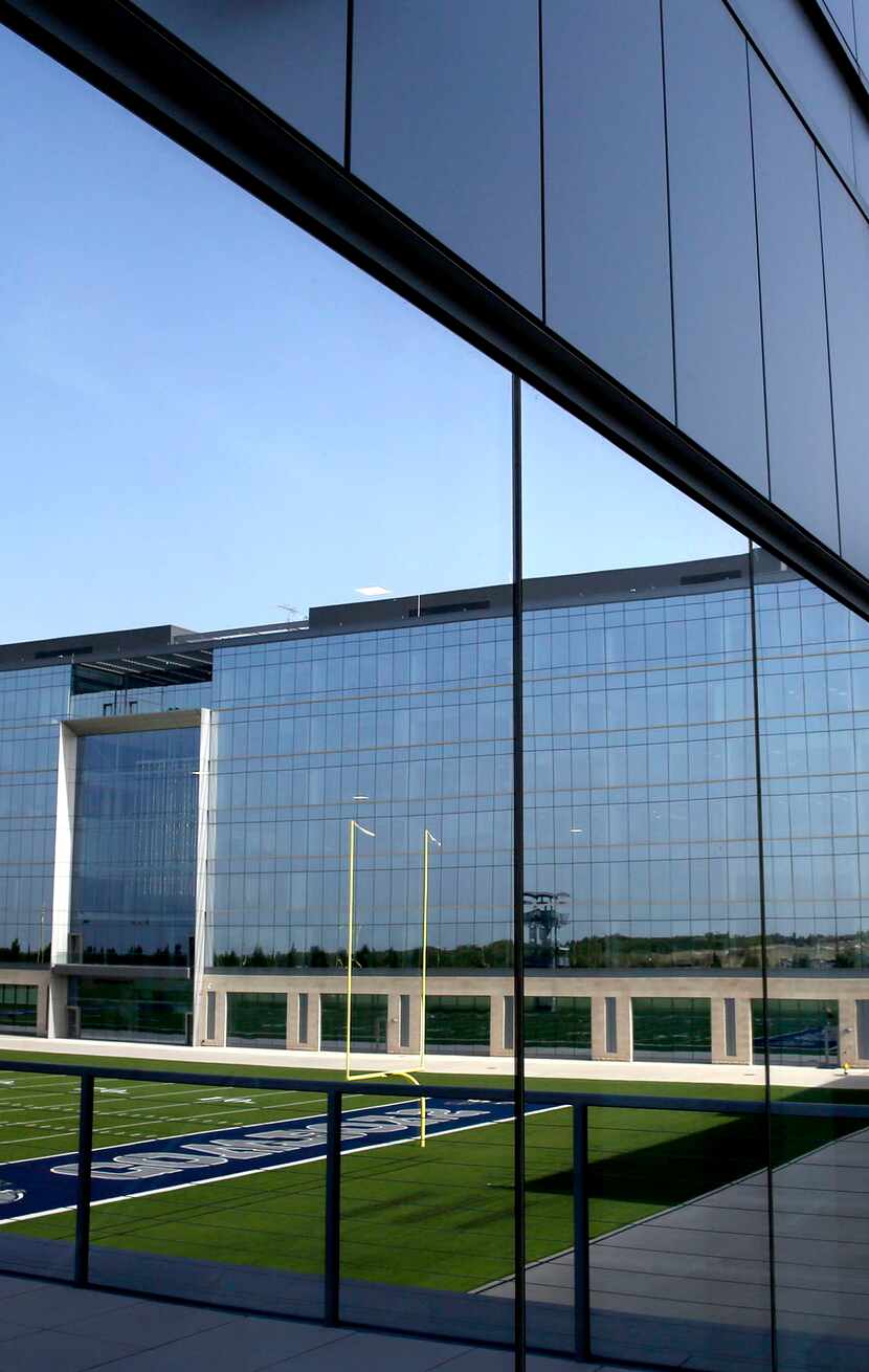 An outdoor practice field is reflected in the glass of the Dallas Cowboys headquarters...