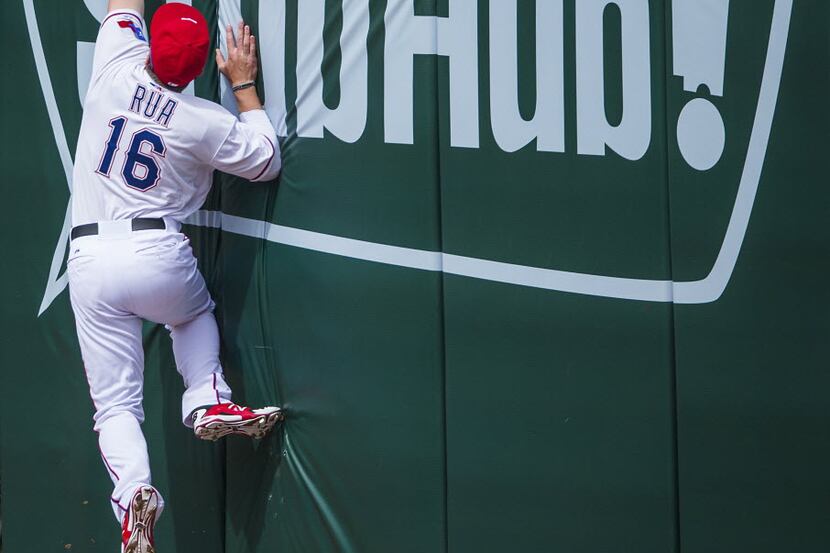 Texas Rangers left fielder Ryan Rua leaps against the outfield wall trying to get to a home...