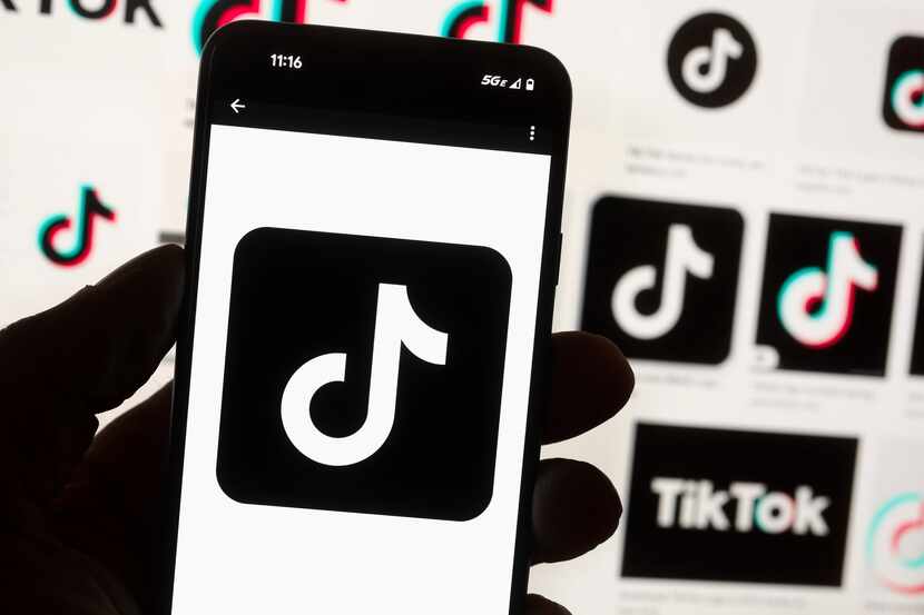 El logotipo de TikTok aparece en la pantalla de un teléfono celular frente al monitor de una...