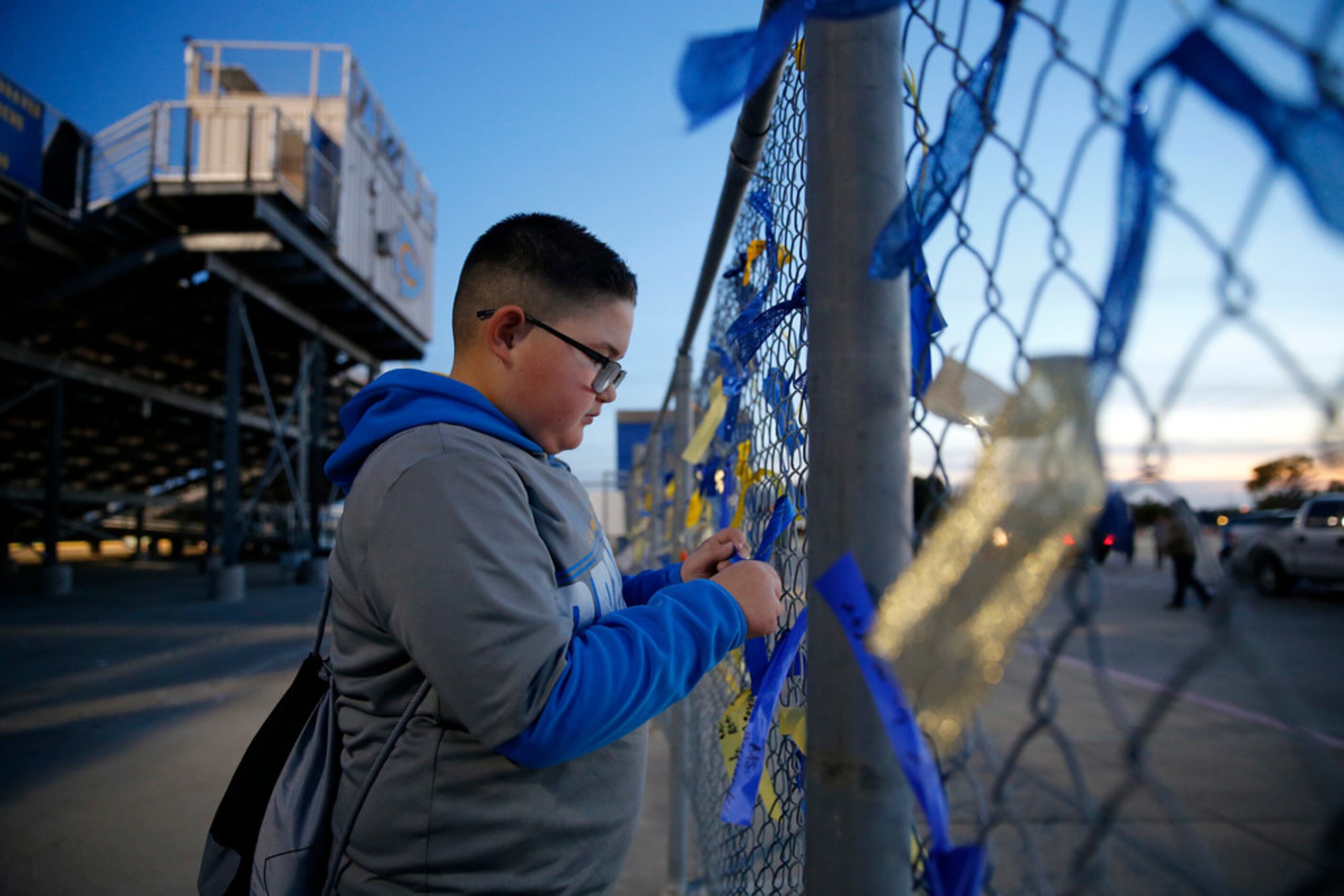 Before the football game, fifth grader Justin Queneau ties a ribbon to the fence in the...