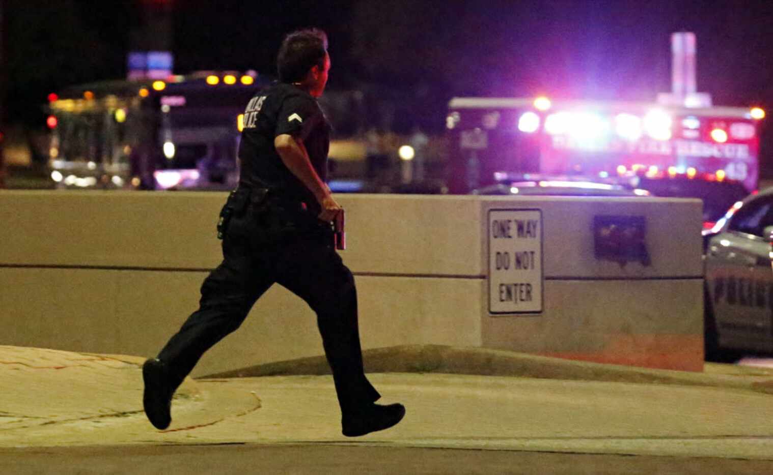 A Dallas police officer runs with his gun drawn during the chaos that followed a deadly...