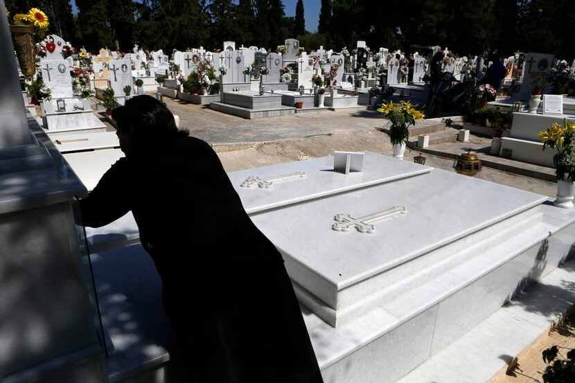 
A woman visits an Athens cemetery, where simpler graves reflect the debt crisis. A mason...