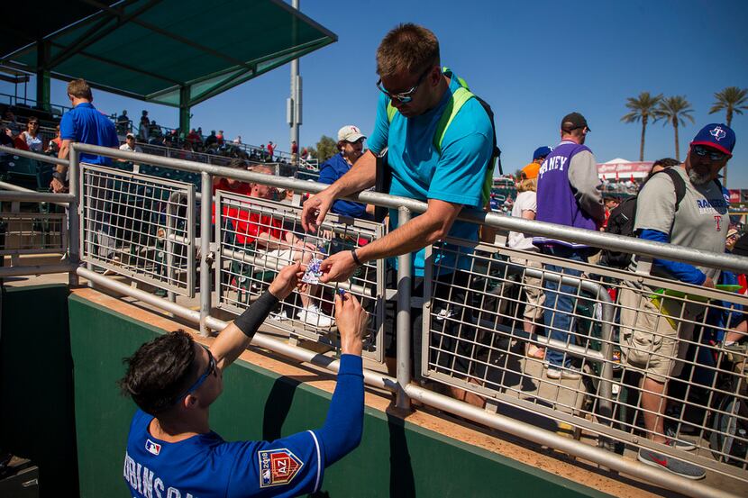 Texas Rangers infielder Drew Robinson signs autographs for fans before a spring training...