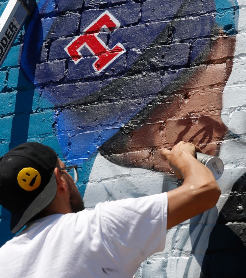 Dallas-based muralist Isaac "IZK" Davies works on the face of Nolan Ryan on the mural he is...