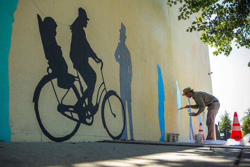 John Kushmaul paints silhouette figures along a wall on South Main Street between 12th and...