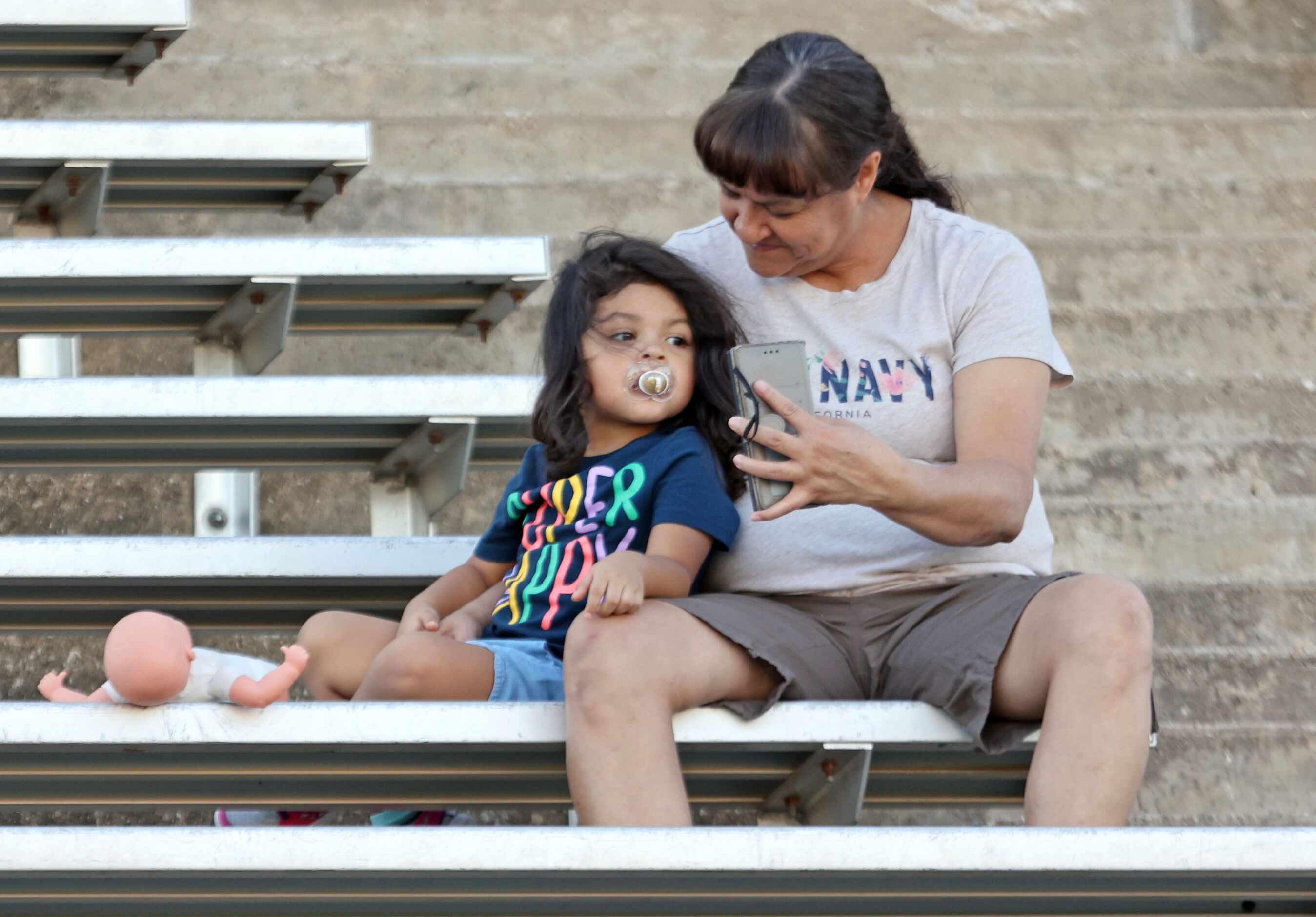 A little girl in the South Garland Stands looks at a photo on her mom’s smart phone before...