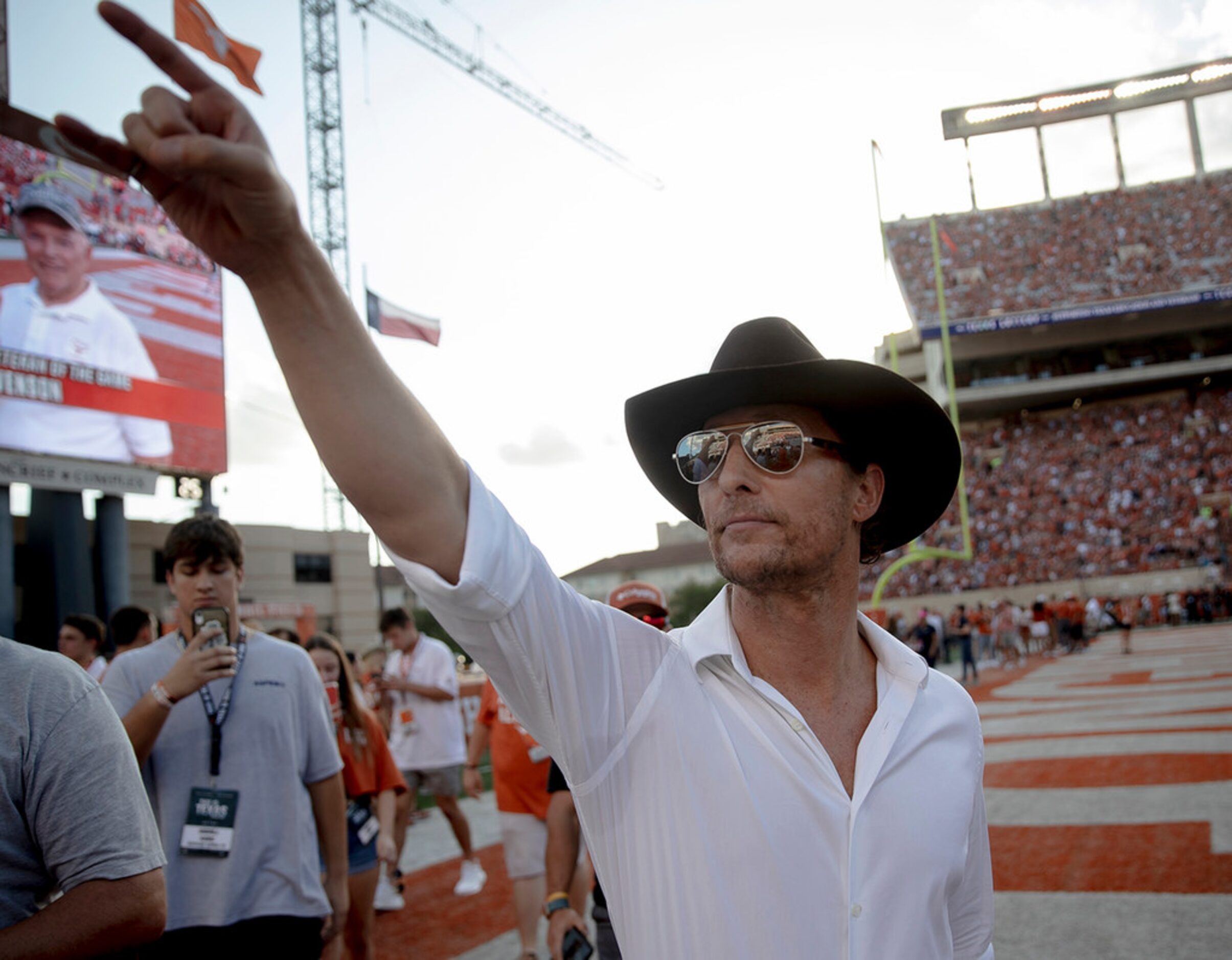 Actor Matthew McConaughey holds up the "Hook 'Em Horns" sign to Texas fans before a game...