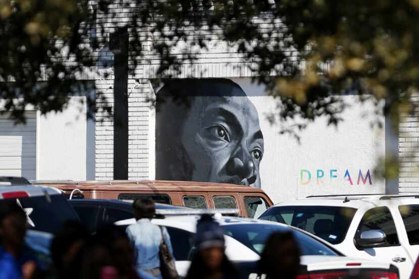 A mural in the likeness of Martin Luther King, Jr. can be seen while people watch the parade...