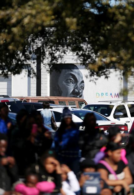 A mural in the likeness of Martin Luther King, Jr. can be seen while people watch the parade...