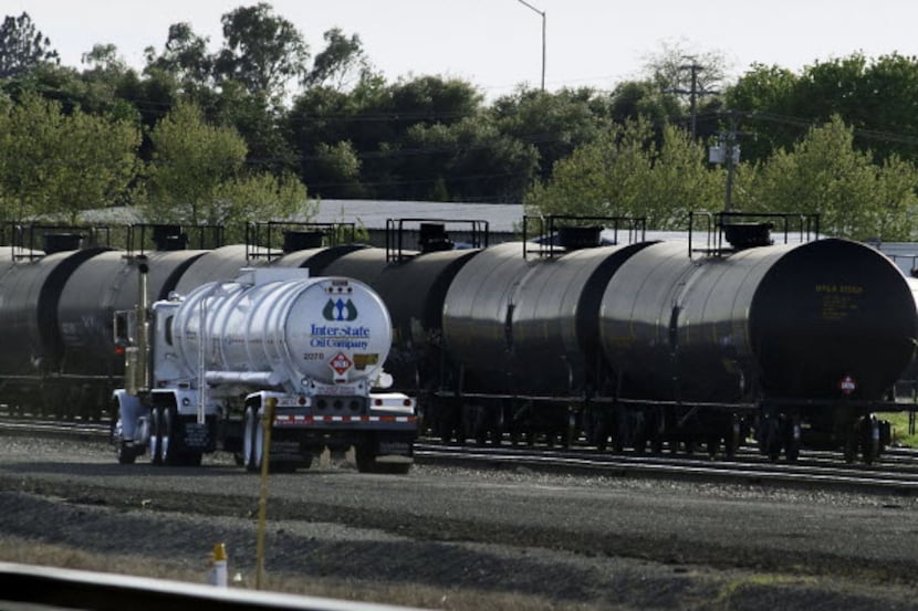Recently filled, a tanker truck drives past railway cars containing crude oil on railroad...
