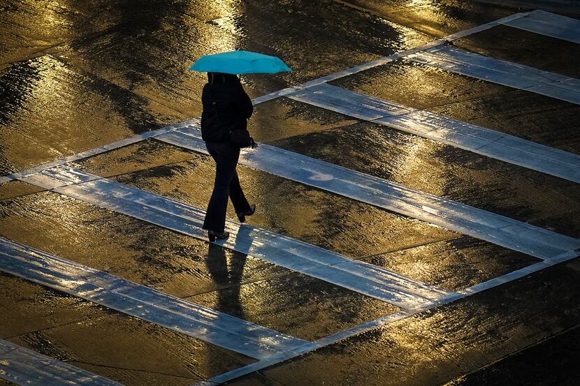 A pedestrian bundles up against rain while crossing Nowitzki Way at Victory Avenue in Dallas.
