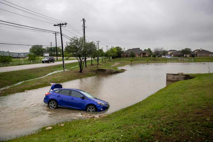 Following a severe storm Thursday night, water rushes past a car whose drive had landed in...