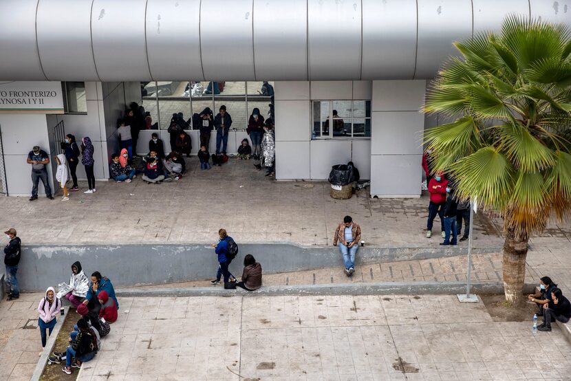 A couple dozen expelled migrant families sit in the plaza near the international bridge...