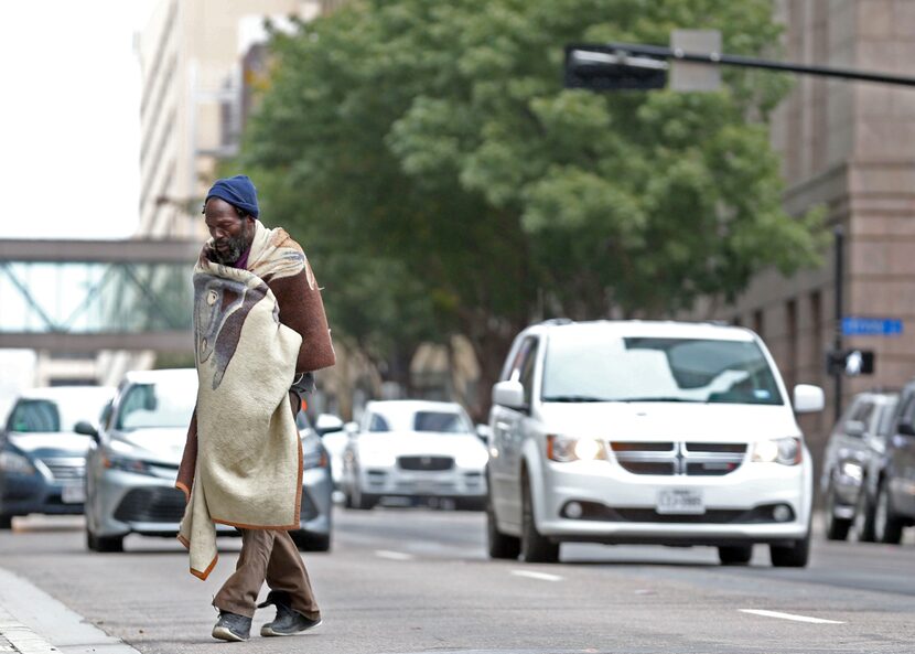 A homeless man wraps himself in a blanket while crossing Elm Street as temperatures drop on...