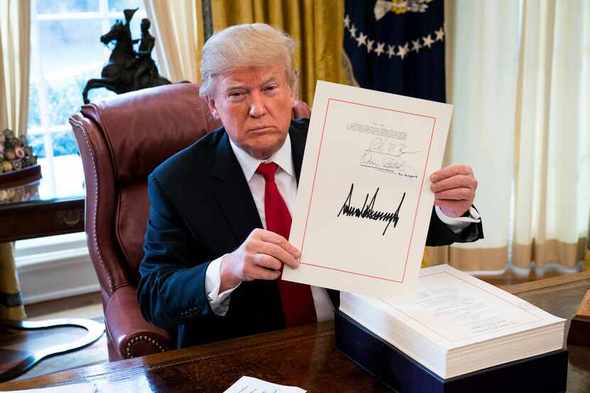 President Donald Trump displays his signature on a sweeping tax bill in the Oval Office of...