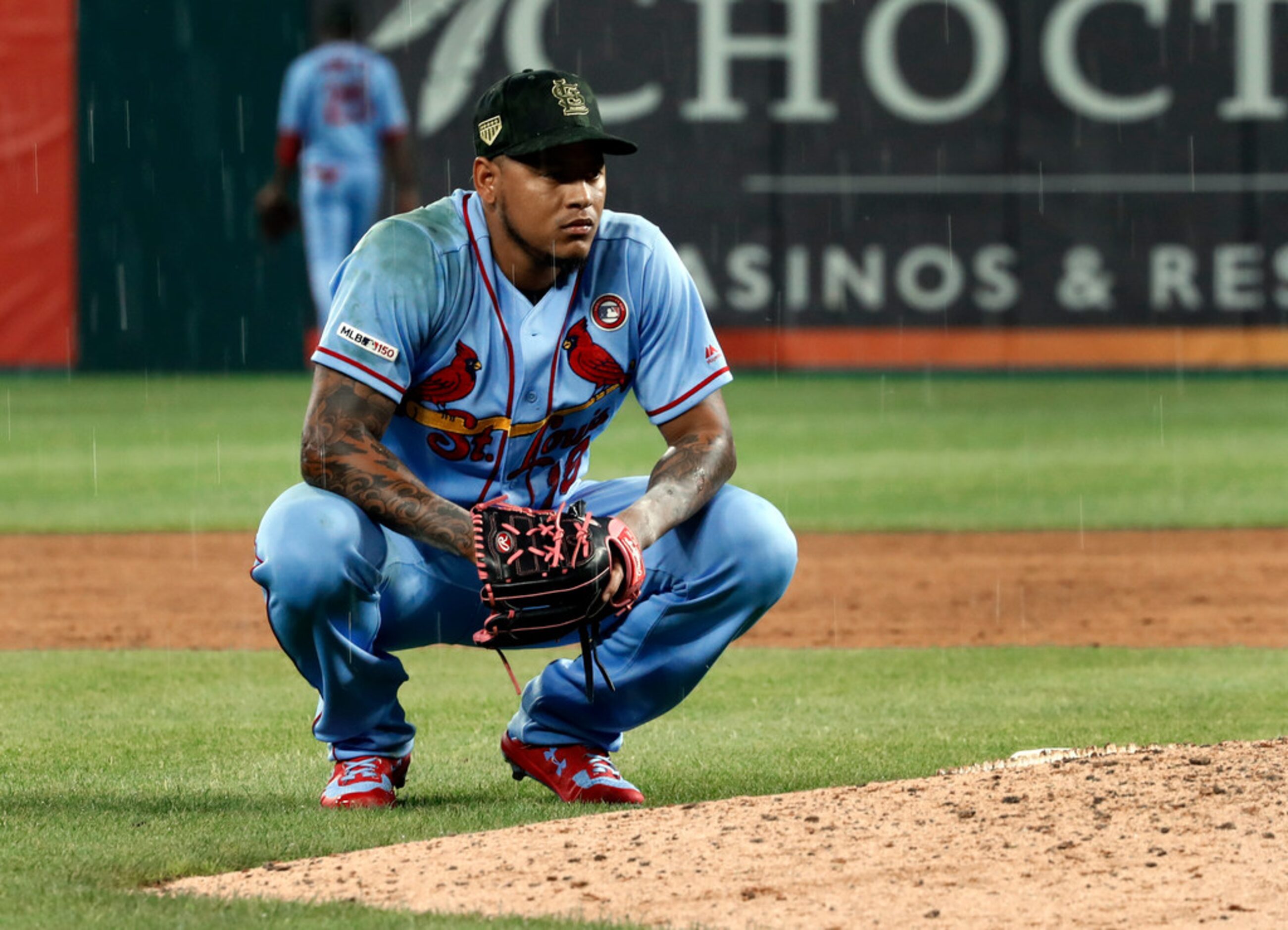 St. Louis Cardinals reliever Carlos Martinez kneels behind the mound as rain begins to fall...