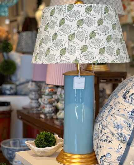 A turquoise blue cylinder-shaped lamp has a shade made of a green-and-white patterned fabric.