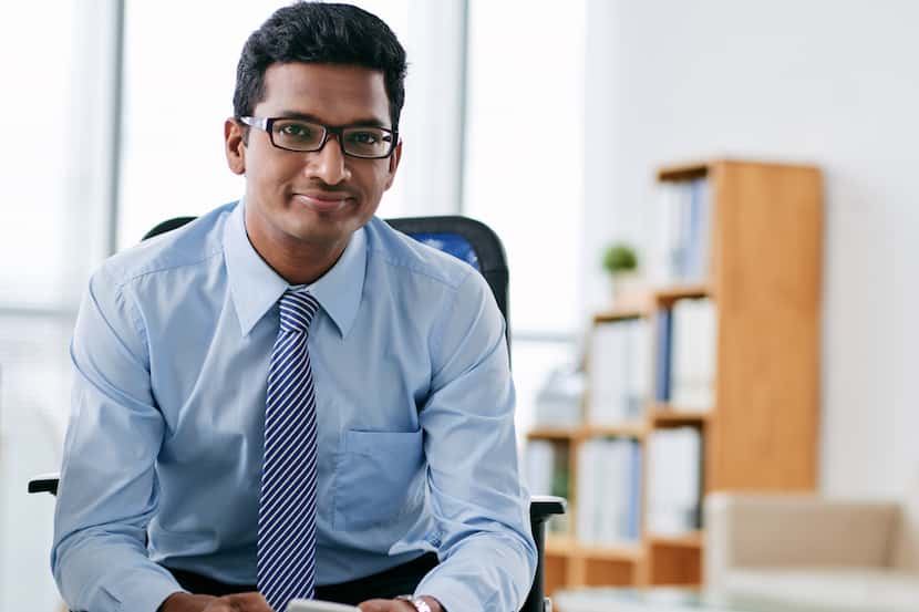 Portrait of smiling Indian business person with smartphone sitting in office.