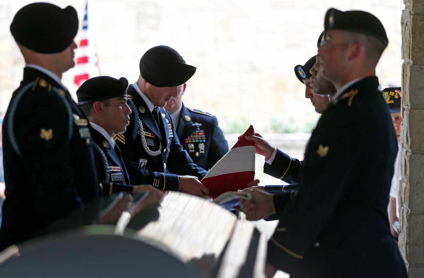 Members of the US Army Honor Guard fold an American flag that has wrapped over a casket of...