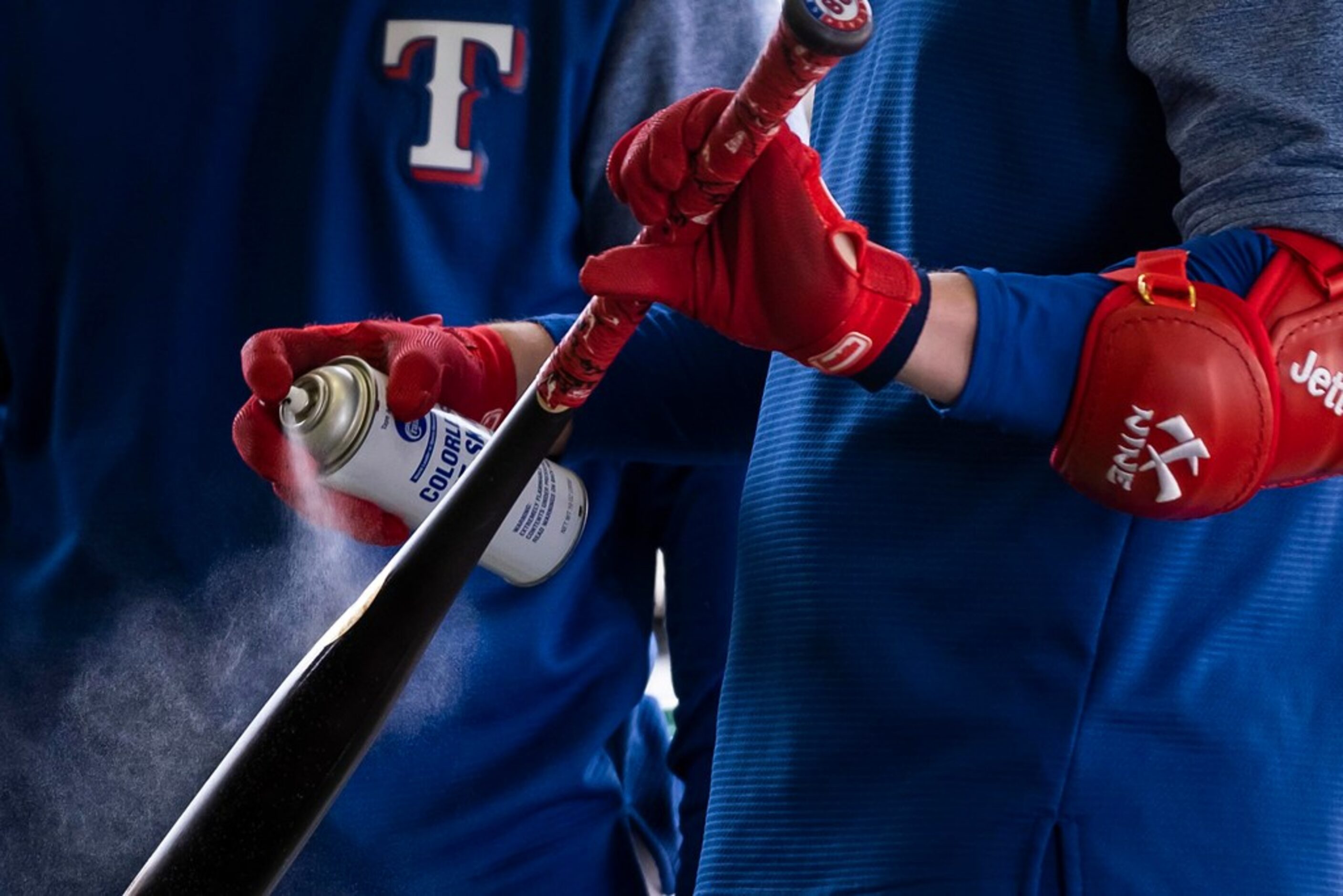 Texas Rangers catcher Jett Bandy spays adhesive on his bat before taking batting practice...