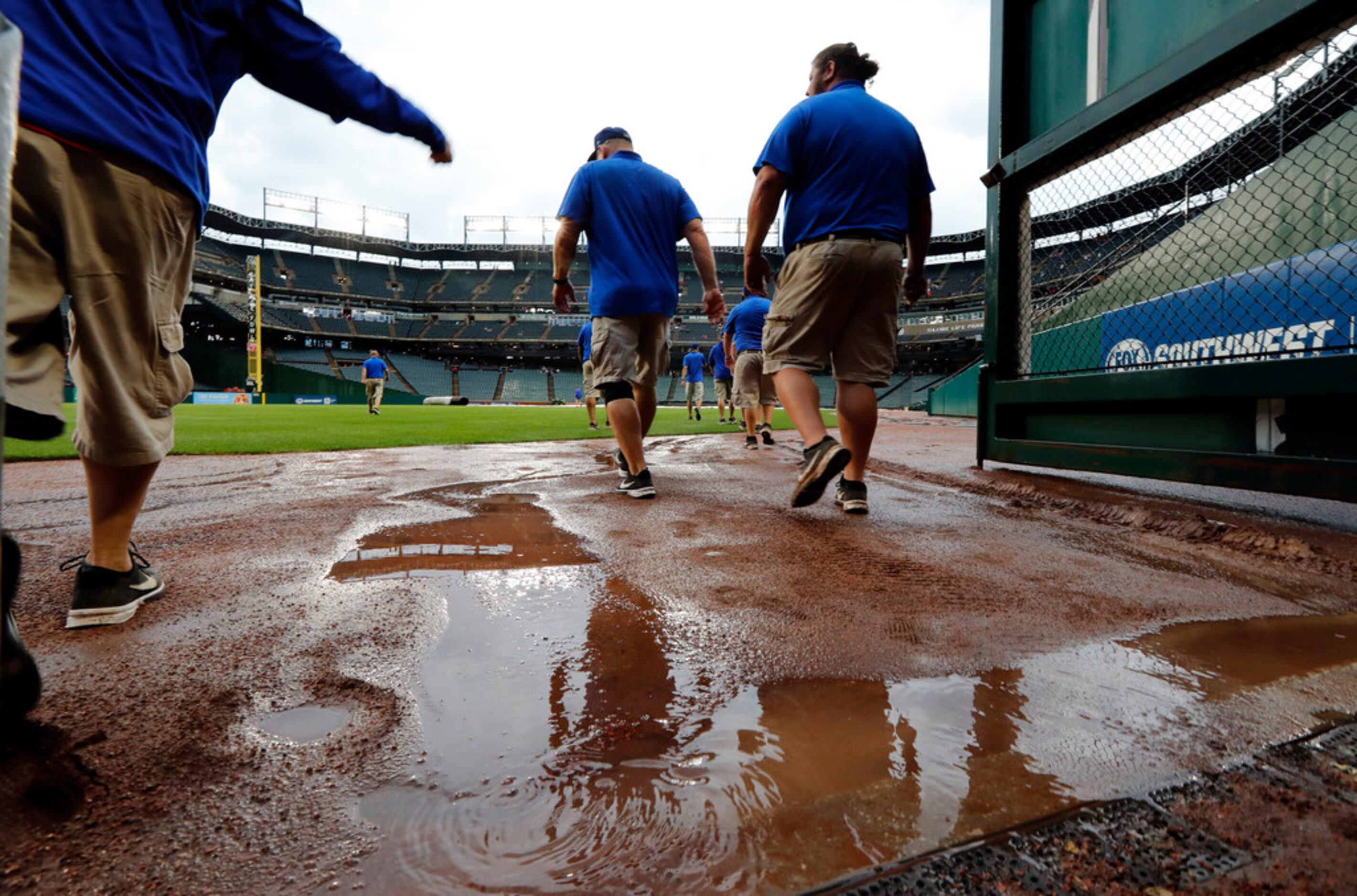 Water lays on the outer track as Texas Rangers grounds crew members head onto the field to...