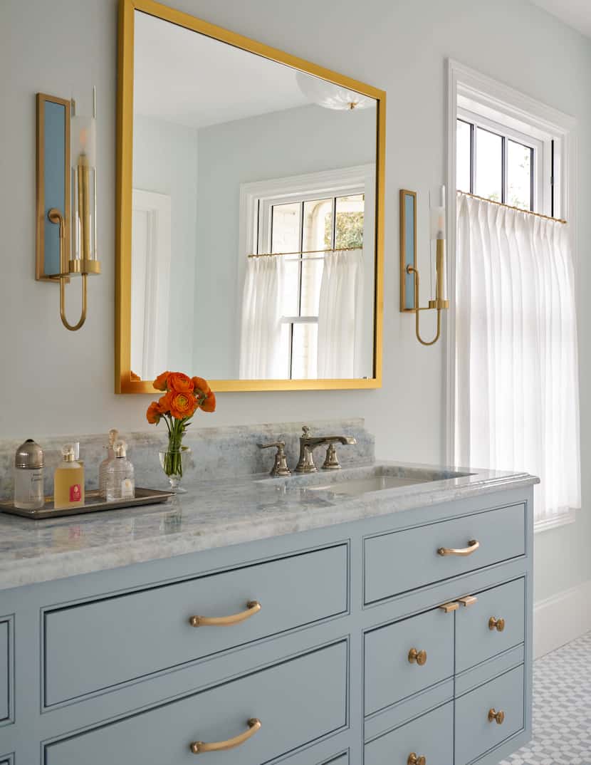 A bathroom features blue cabinets, a gold mirror and a stone countertop.