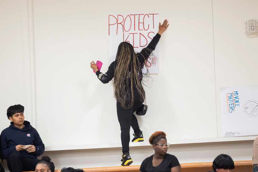 A student tapes a sign that reads “Protect kids not guns” to the wall before an assembly for...