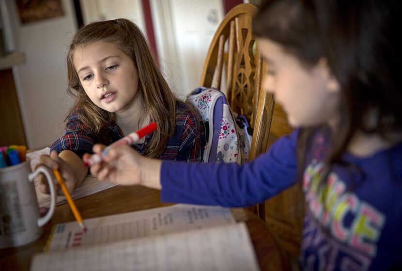 
Molly Kahlig (left) helps her sister, Lucy, with a math problem. The children eat...