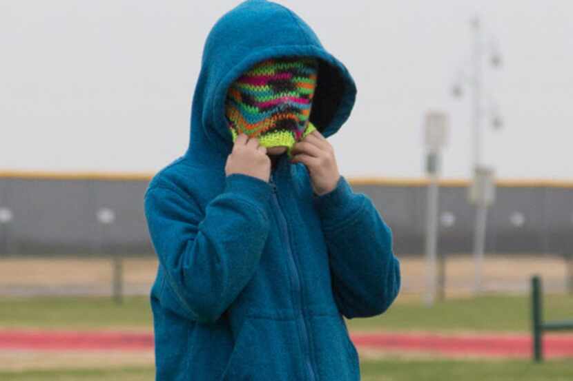 Colin Stokes covers his face with his beanie to keep warm while he plays soccer with other...