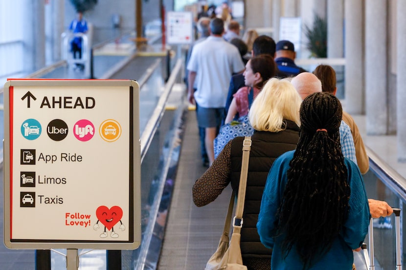 People make their way along a moving walkway to the new pickup location for Uber, Lyft and...