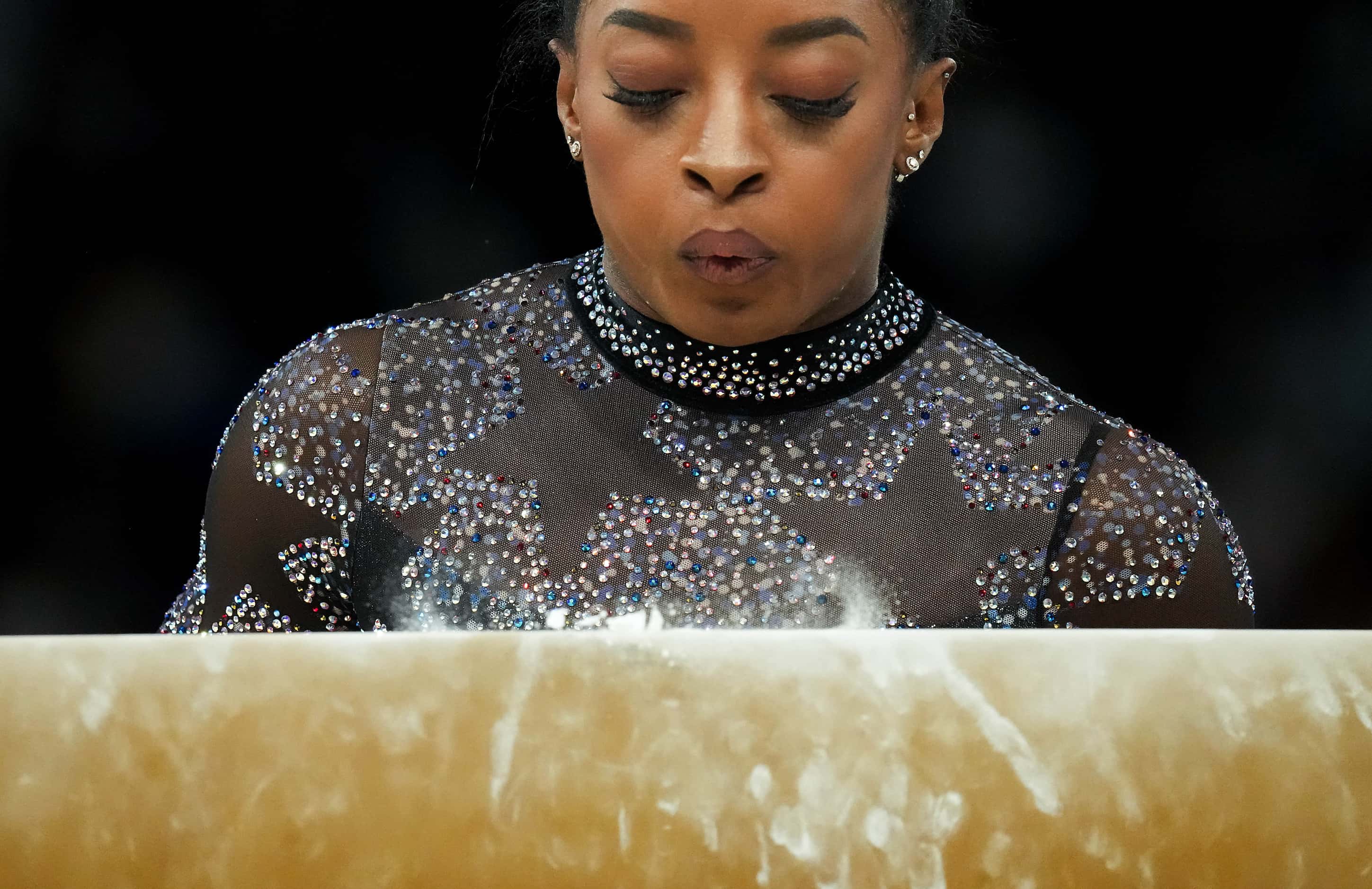 Simone Biles of the United States blows chalk from from the apparatus before she competes on...