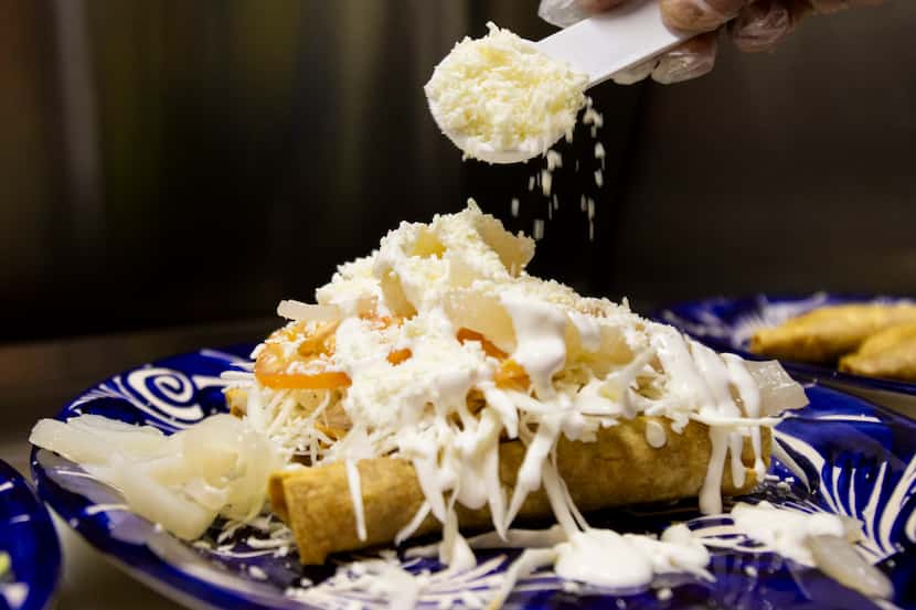 Cheese is sprinkled on a plate of Tacos Dorados Estilo San Juan at Maskaras Mexican Grill in...