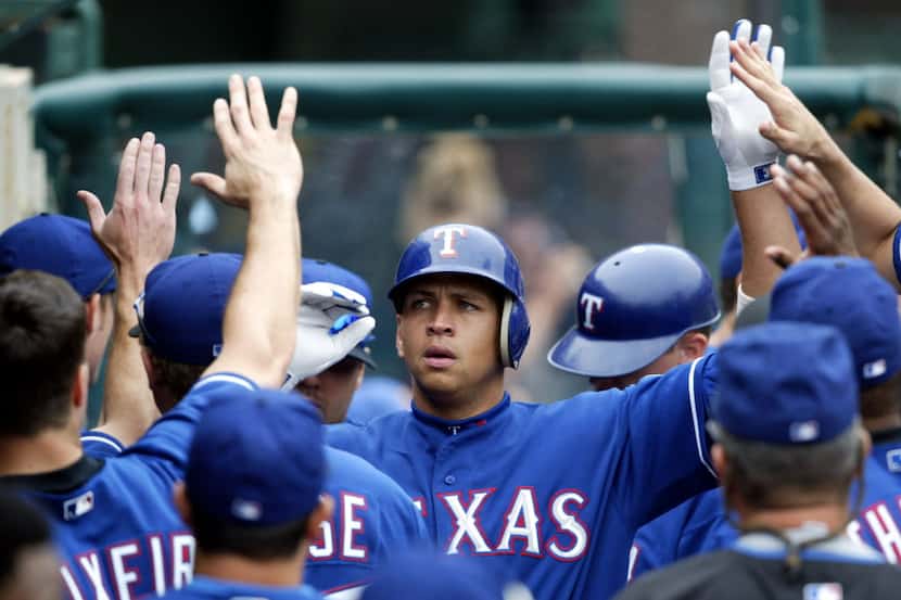 Texas Rangers' Alex Rodriguez is greeted in the dugout after scoring on Rafael Palmeiro's...