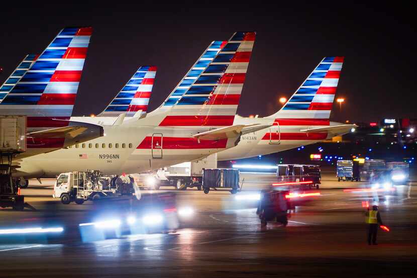 Baggage carts pass American Airlines planes at the gates of Terminal C at DFW Airport on...