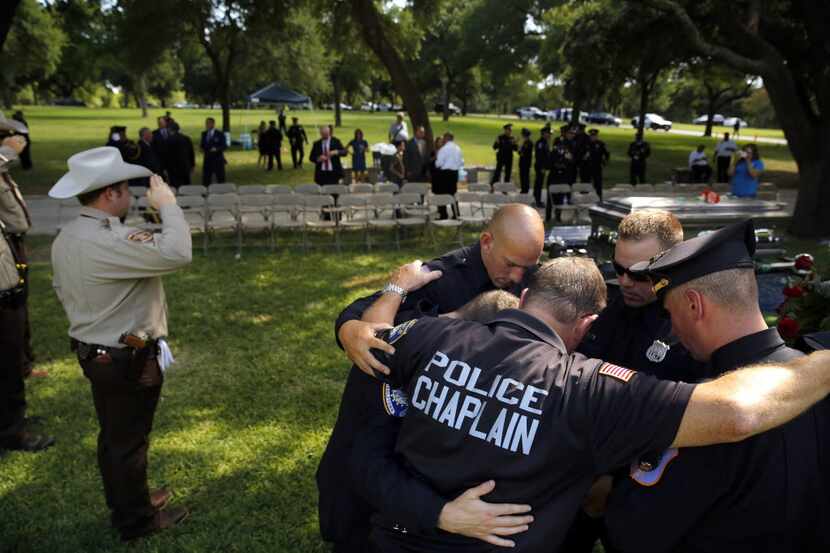 A police chaplain and officers from out of state pray following a graveside service for a...