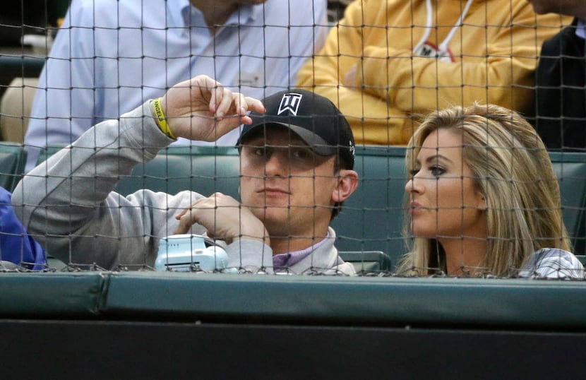 Cleveland Browns quarterback Johnny Manziel, left, sits in the stands during a baseball game...