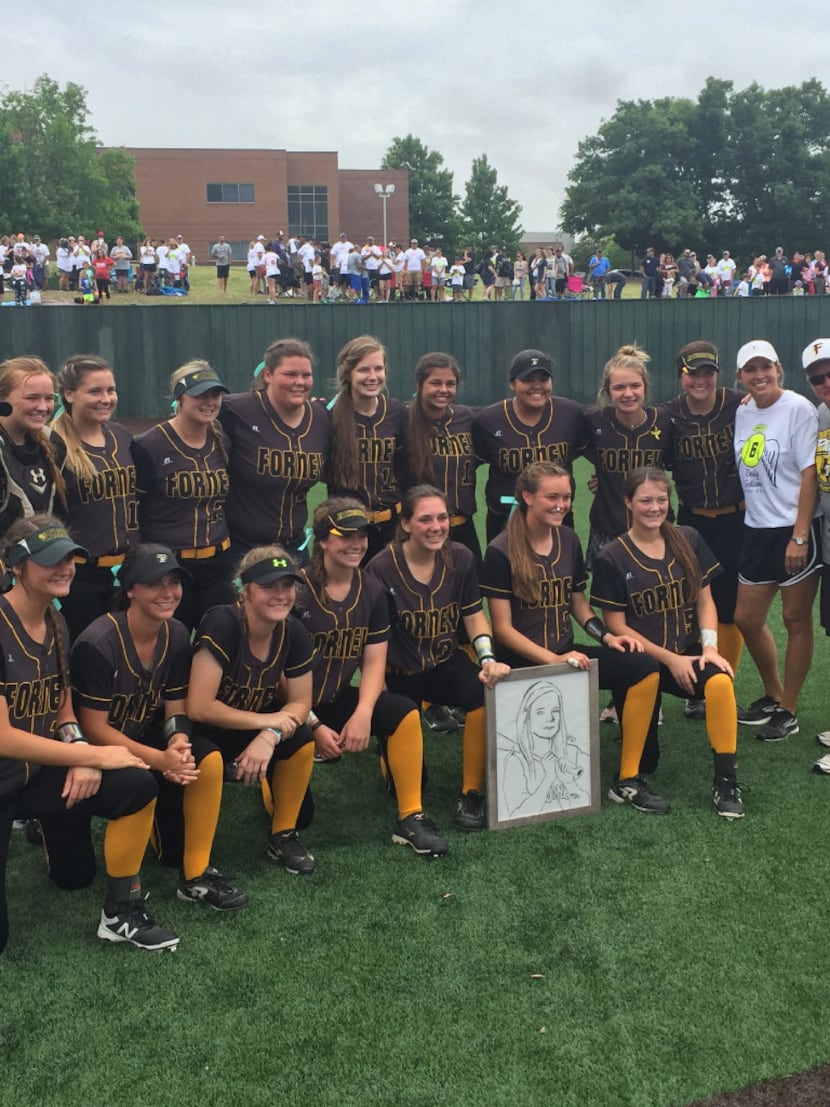 The Forney softball team poses for pictures after Saturday's game while holding a picture of...