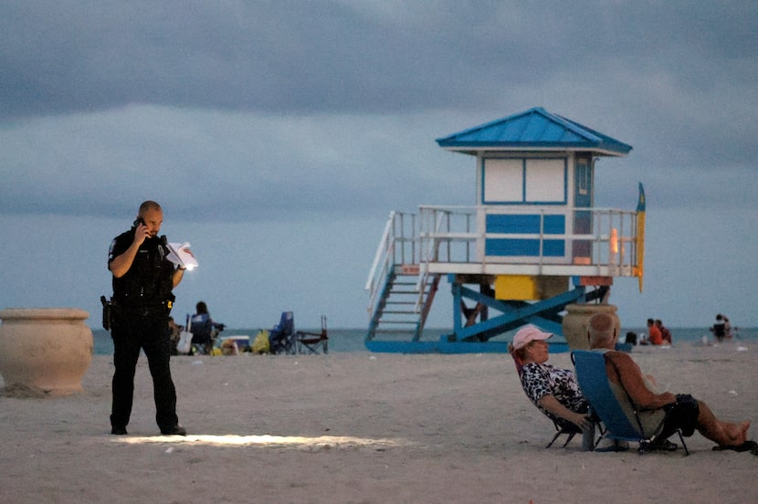 A police officer shines his flashlight downward as he pauses on Hollywood Beach while...