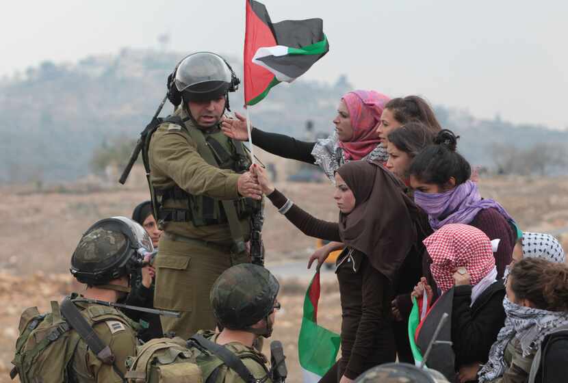  An Israeli soldier gestures to female protesters to move away during a demonstration...