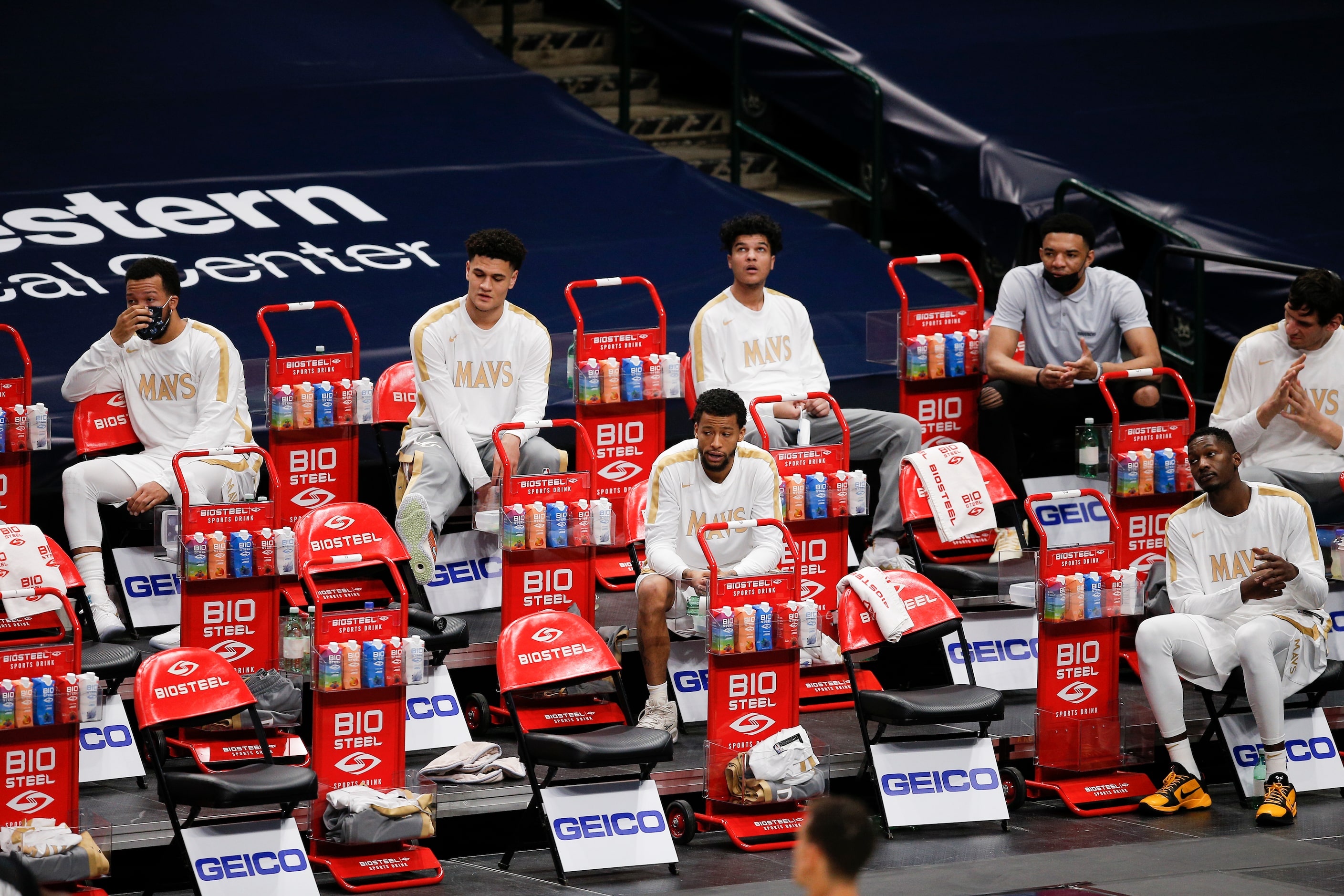 The Dallas Mavericks reserve players sit socially distanced on the sidelines during the...