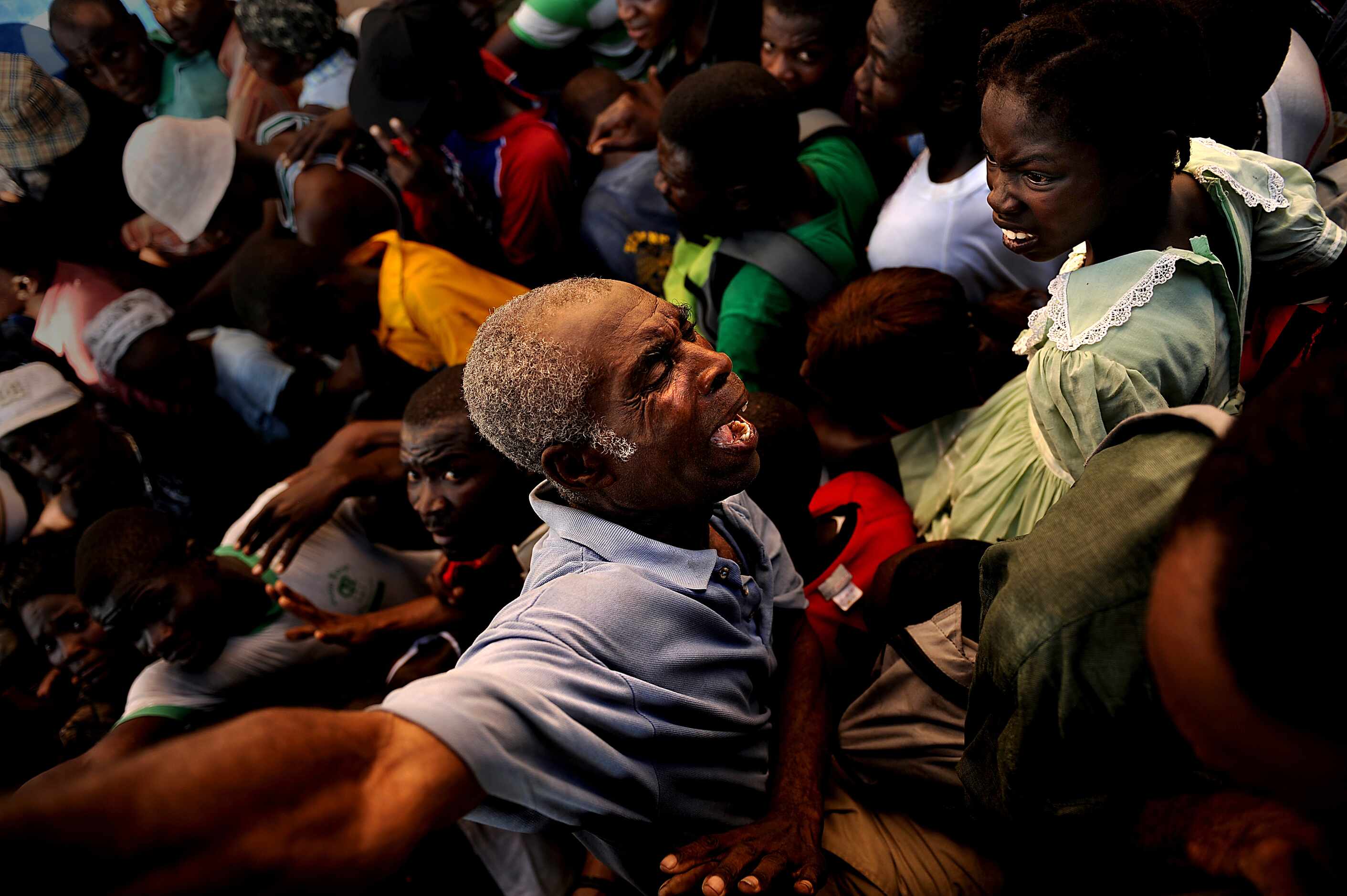An older man is squished while he tries to get out of the way of a huge number of Haitians...