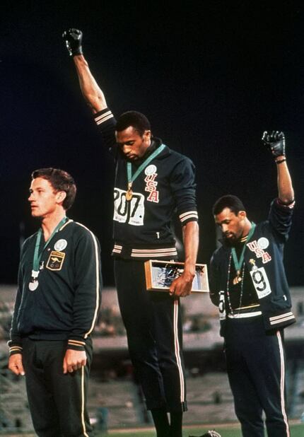U.S. athletes Tommie Smith (center) and John Carlos (right) raised their gloved hands in...
