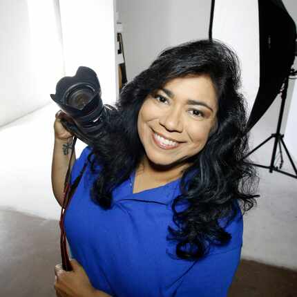 Photographer Debra Gloria poses in her studio while holding a camera.