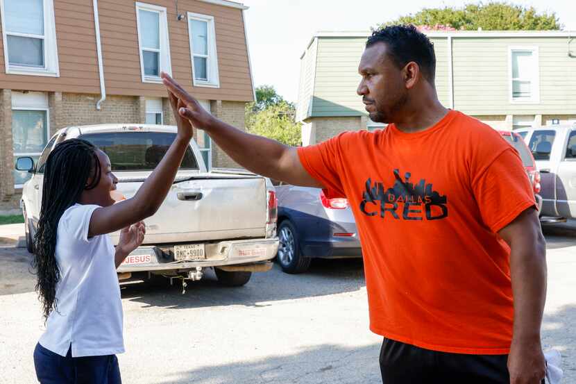 Kendall White, 10, high-fives Victor Alvelais of Dallas CRED while talking with residents of...