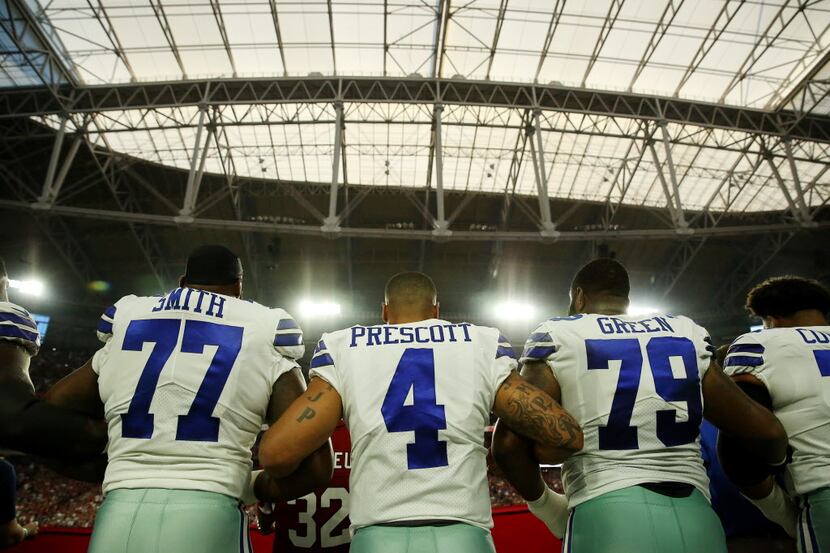 Dallas Cowboys quarterback Dak Prescott (4) locks arms with teammates during the playing of...