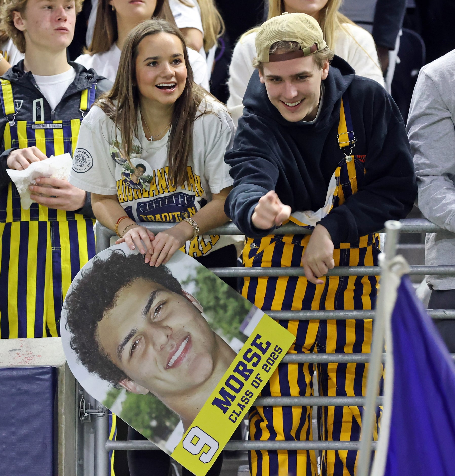 Highland Park High student fans joke with cheerleaders on the sideline, while holding a head...