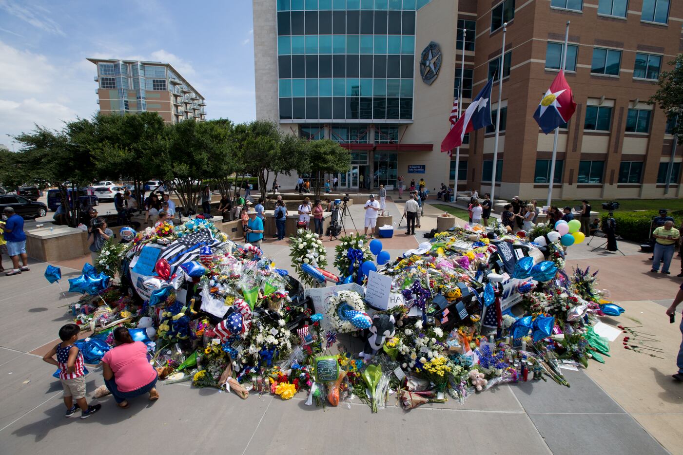 By July 9, two Dallas police cars were buried so deep in flowers and mementos that they...