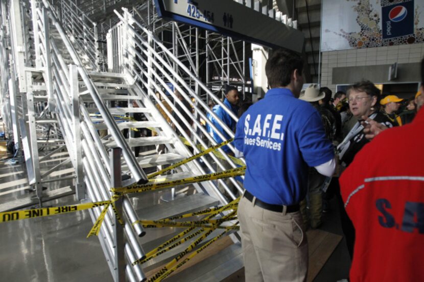 Security personnel speak with fans while construction workers try to ready the temporary...