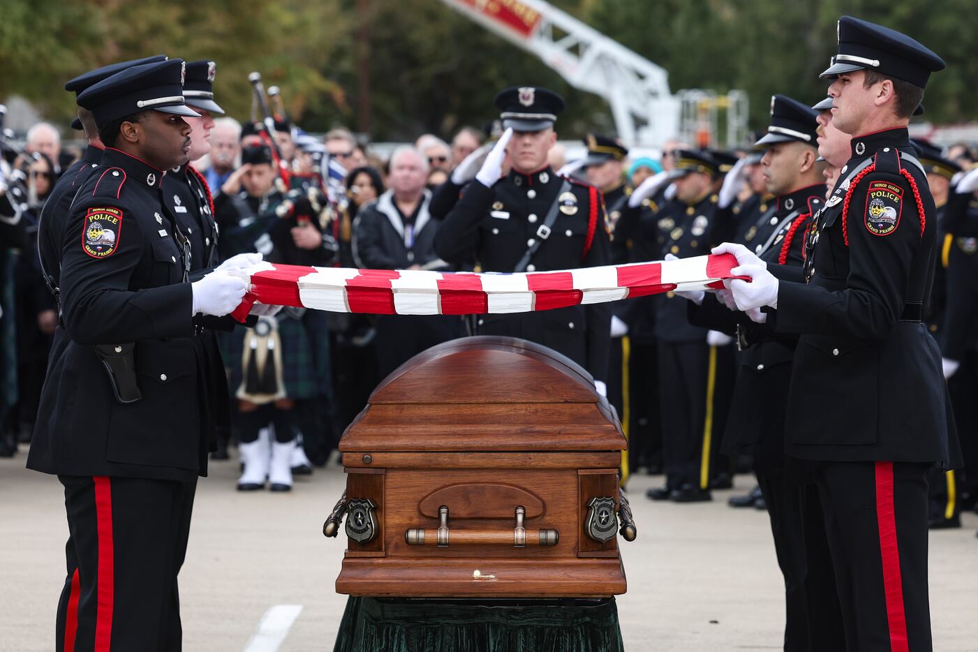 Grand Prairie Police Department Honor Guard members hold an American flag above the casket...